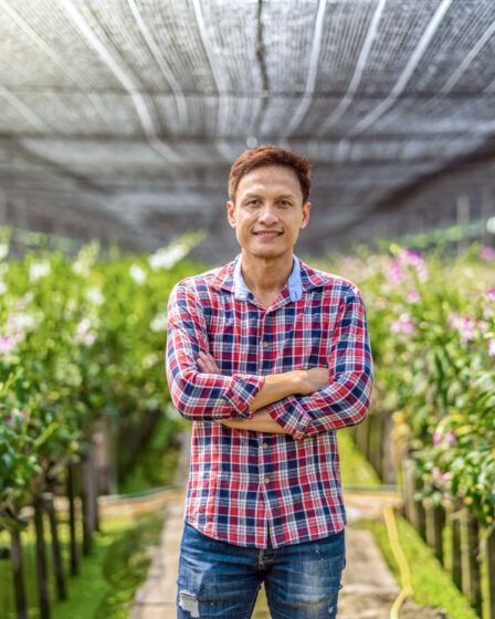 Asian small business owner and orchid gardener in greenhouse illustrating starting a farm.