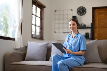 Young Asian nurse or caregiver with tablet, assisting elderly at home.