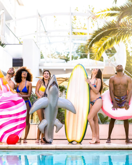 Group of friends enjoying a pool party with floats and surfboards.