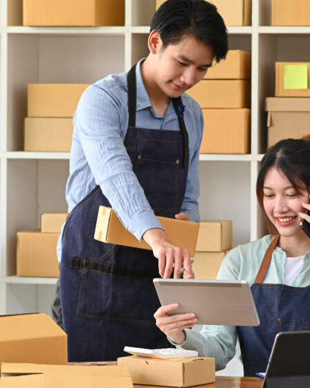 Young Asian couple starting a small business, working with boxes and tablet.