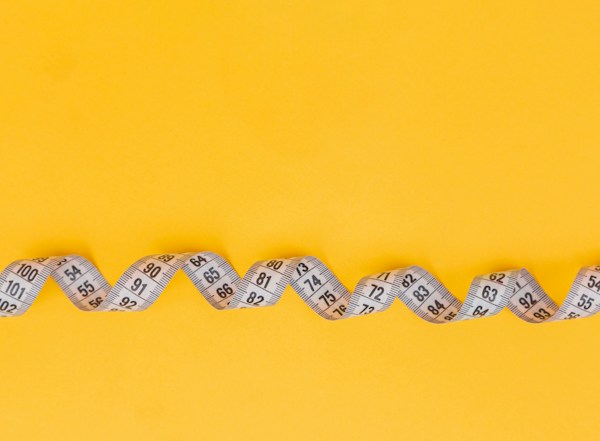 Measuring tape on yellow background illustrating healthy weight loss and diet.