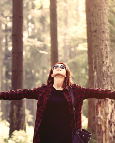 Woman with arms outstretched in forest, embracing personal growth and self-reflection.