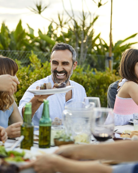 Man smiling with barbecue food and drinks at a family gathering.